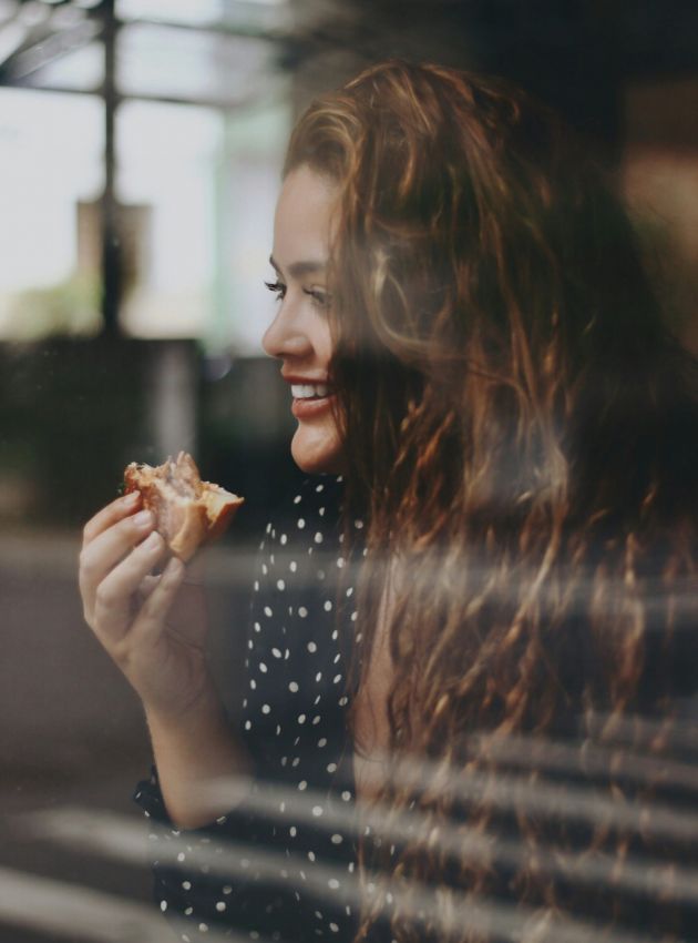 Woman sitting in a restaurant window smiling and eating a sandwich